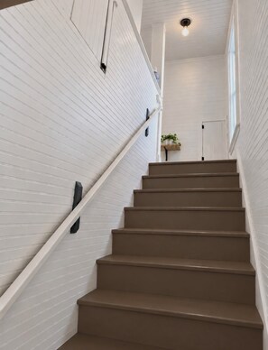 A staircase with white paneling and brown steps, leading to a landing with a plant. - Near IU Stadium and Downtown- 6 Beds (Bloomington)