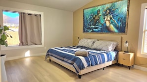 Een slaapkamer met een bed, nachtkastje, schilderij, raam met gordijnen en een plant.