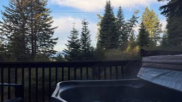 A hot tub on a wooden deck with a view of tall trees and a clear sky.