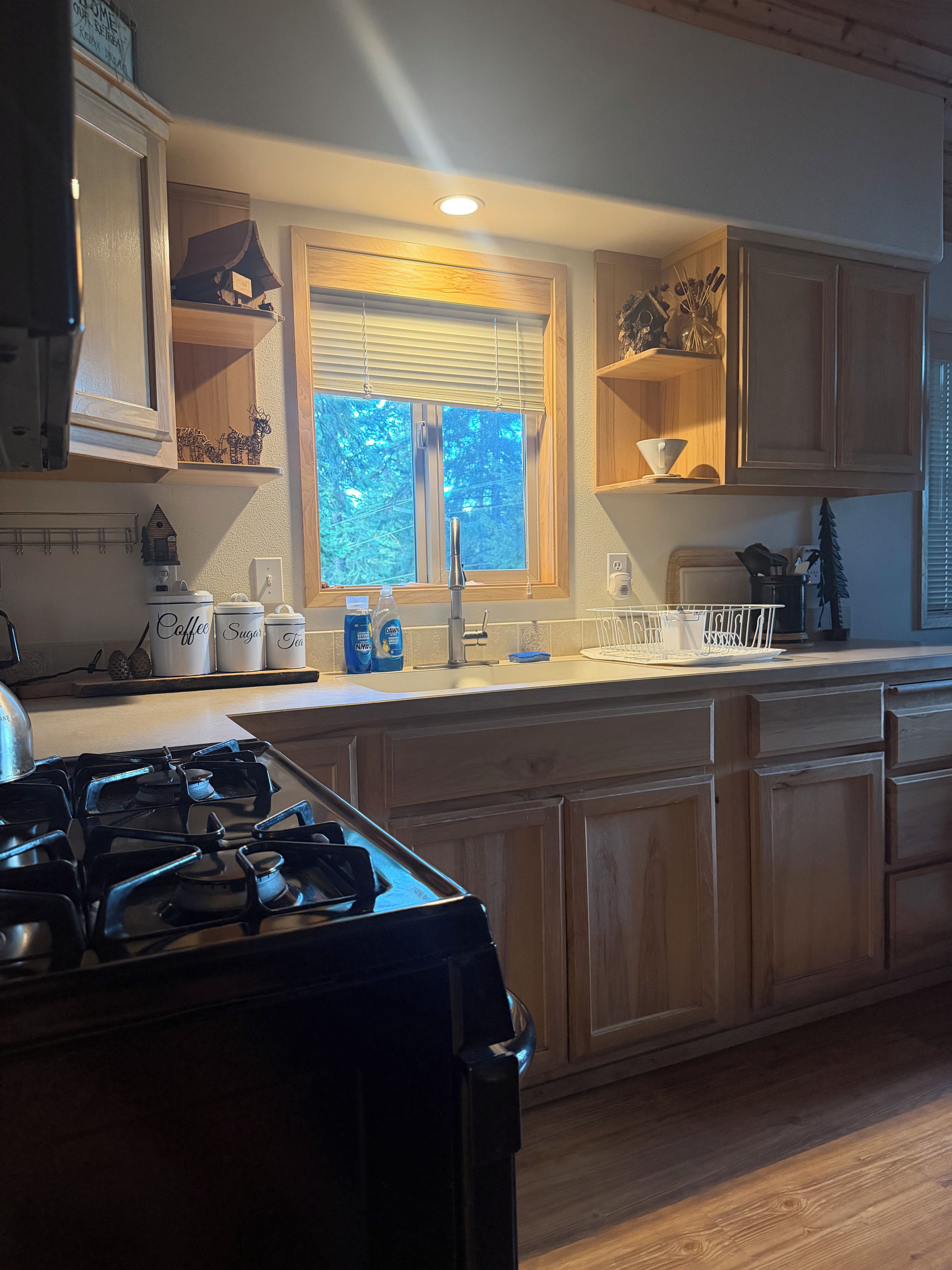 A kitchen with wooden cabinets, a stove, a window with blinds, and various kitchen items on the counter.
