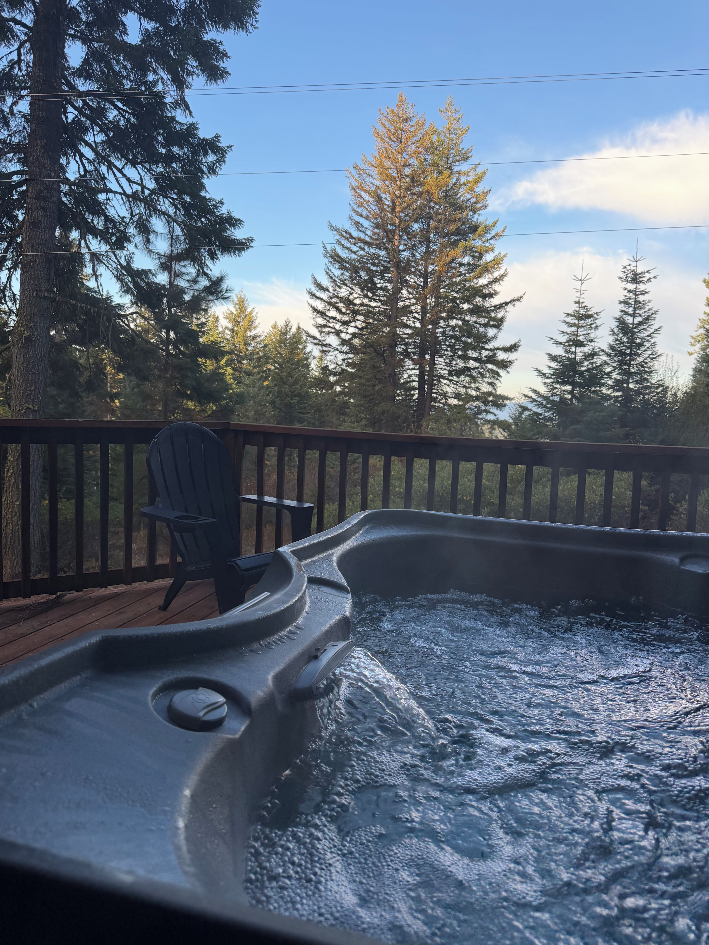 Un bain à remous sur une terrasse en bois, avec une chaise, entouré d’arbres.