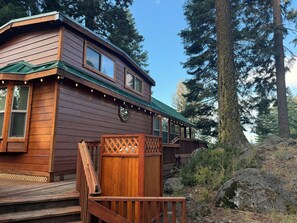 A wooden cabin with a deck, surrounded by tall trees.