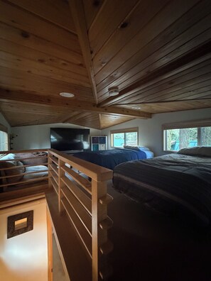 Ein Schlafzimmer mit Holzboden, einem Bett, einem Fernseher und einem Fenster.