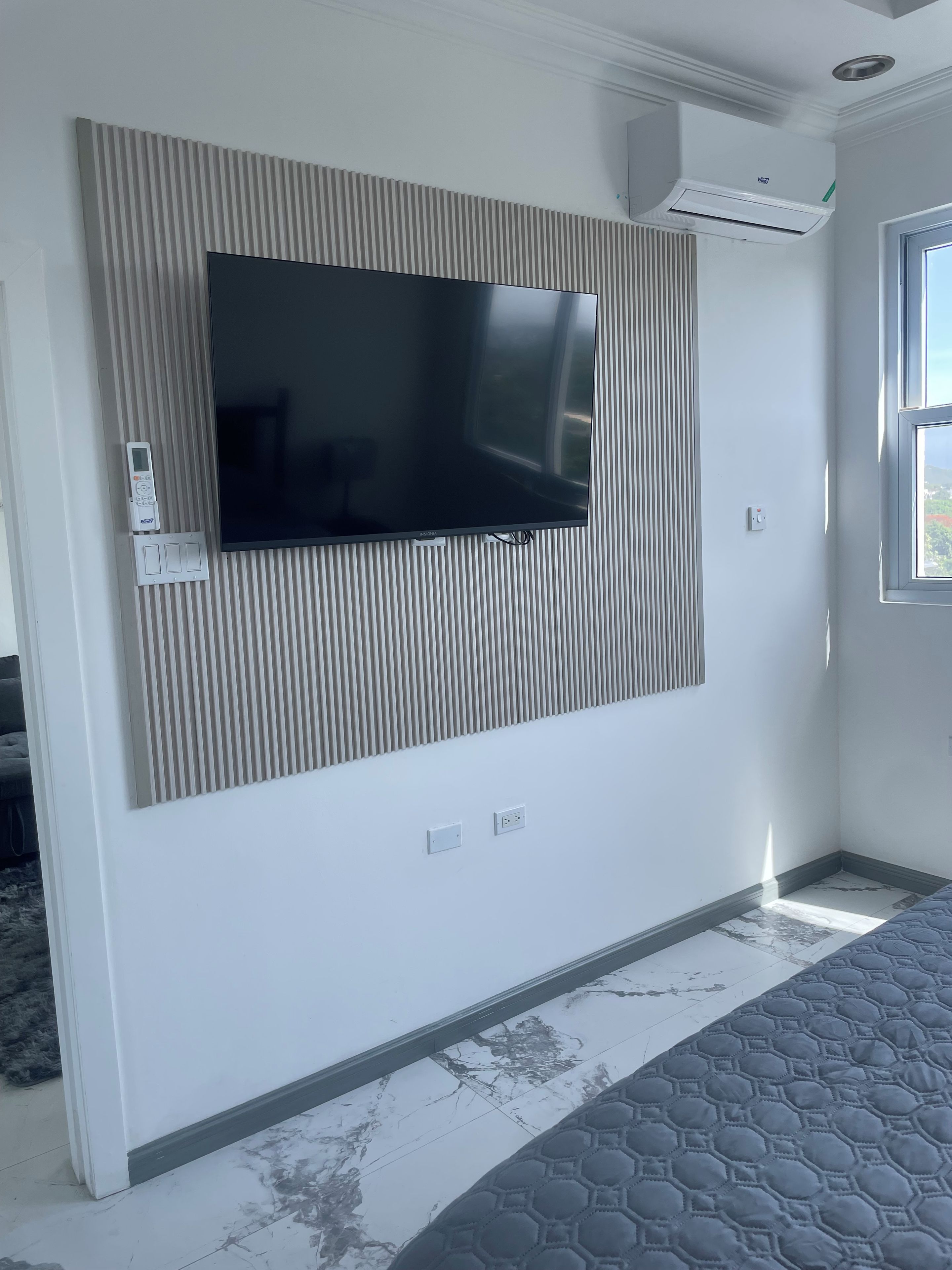 Ein modernes Zimmer mit Flachbildfernseher an einer Wand mit Strukturpaneel, einem Fenster mit Blick und einer Decken-Klimaanlage.