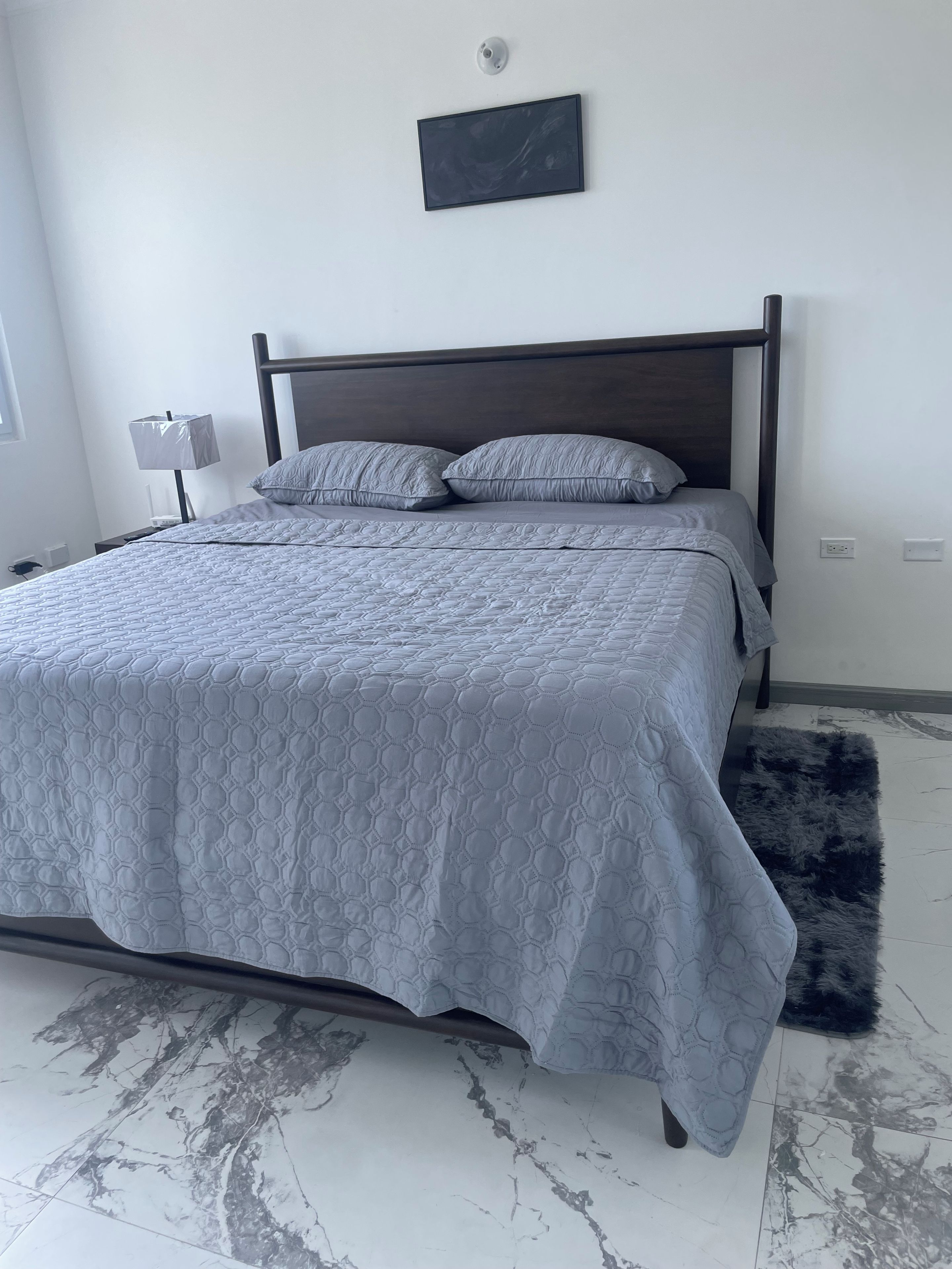 Un dormitorio con cama, mesita de noche, lámpara e iluminación en la pared.