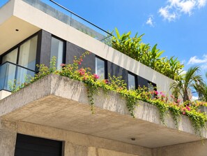 Un bâtiment moderne doté d’un balcon orné de plantes en fleurs, avec un ciel bleu dégagé.