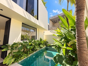 A modern building with a swimming pool surrounded by lush greenery. - Villa Aurora By Aura (Badung)