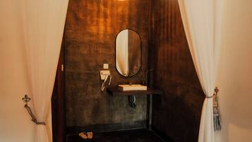 A room with a dark floor, a wooden vanity with a mirror, a small sink, and a telephone. There is a light fixture on the ceiling and a rug on the floor.