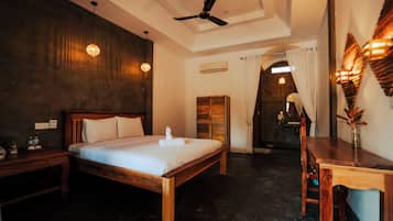 Quarto de hotel com cama de madeira, escrivaninha e ventoinha no teto.