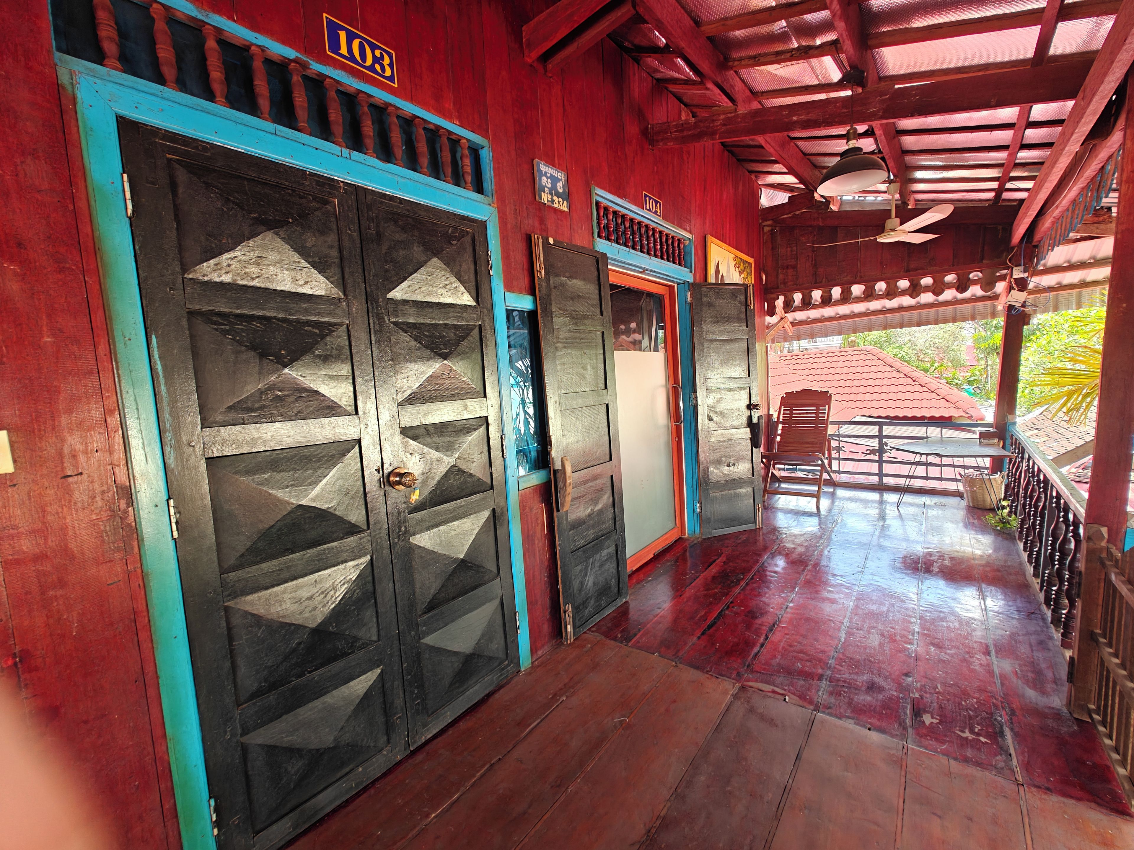 Corredor com portas de madeira, ventilador de teto e vista para o exterior.