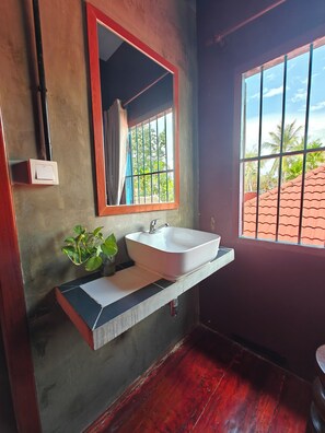 Un baño con un lavamanos blanco, un espejo con marco rojo y una ventana con barrotes.