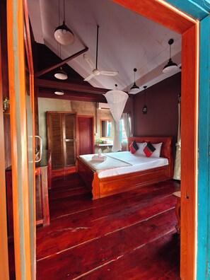 Ein Schlafzimmer mit Holzbett, großem Bett, Holzschrank und Deckenventilator.