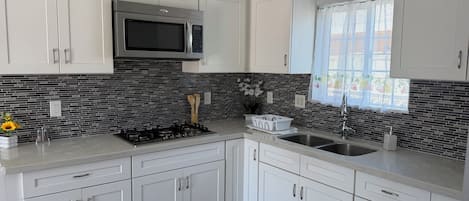 A modern kitchen with white cabinets, a stainless steel microwave, and a black tiled backsplash.