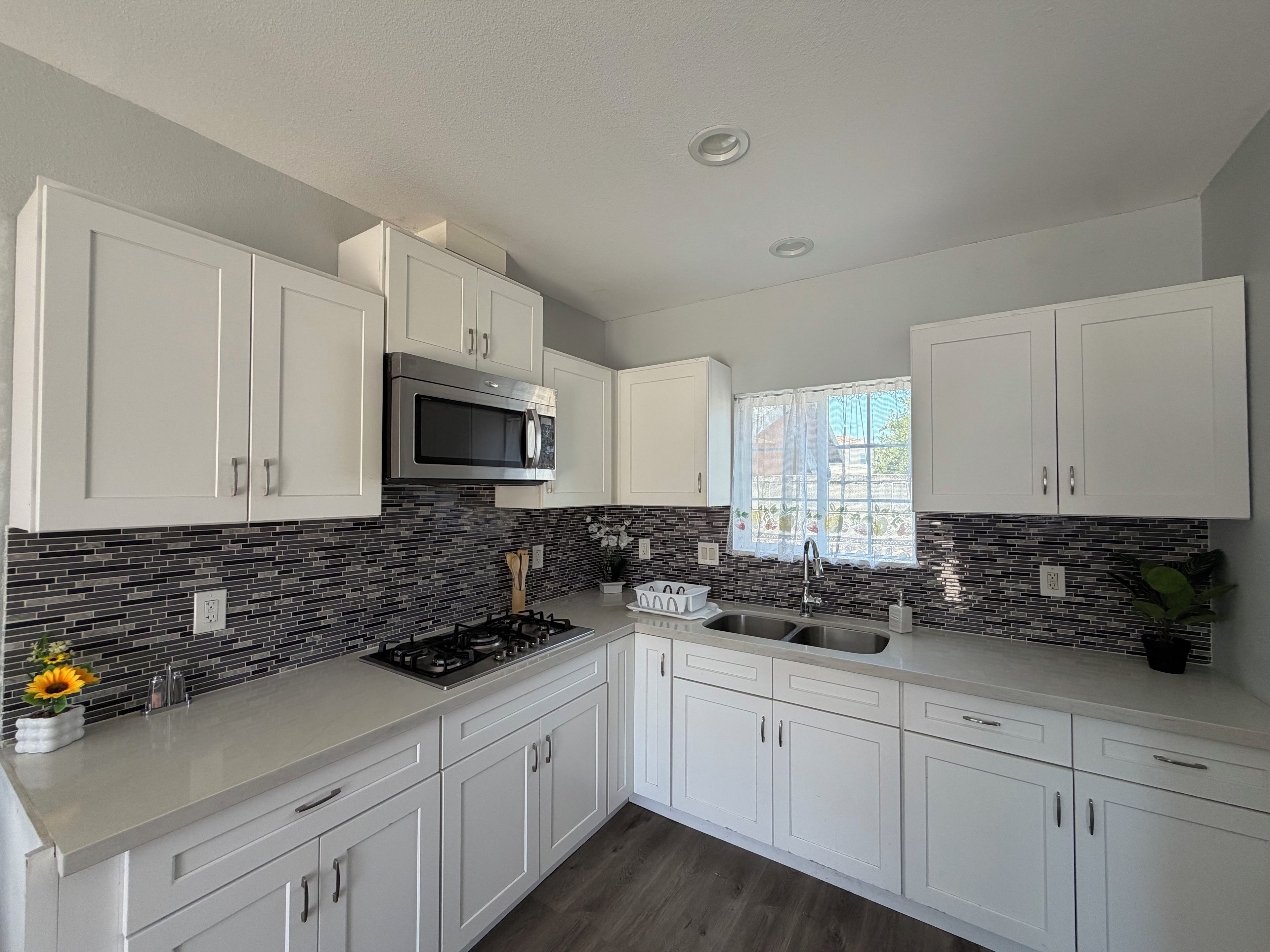 A modern kitchen with white cabinets, a stainless steel microwave, a gas stove, and a window with a view.