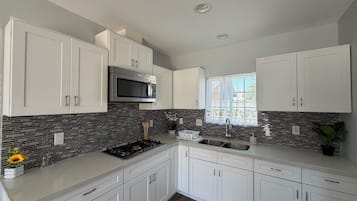 A modern kitchen with white cabinets, a stainless steel microwave, a gas stove, and a window with a view.