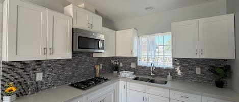 Una cocina moderna con armarios blancos, un microondas de acero inoxidable, una estufa a gas y un ventanal con vistas.