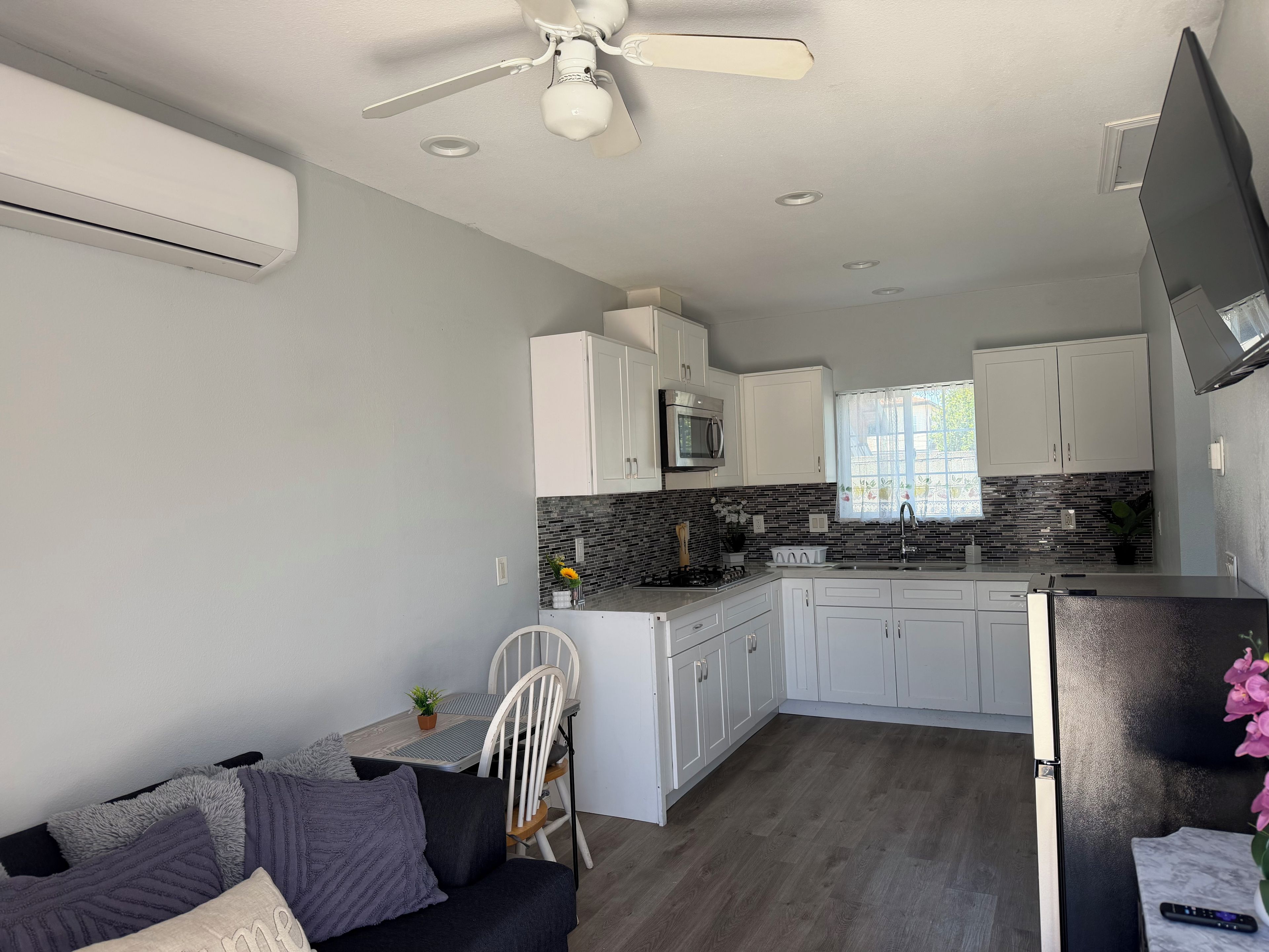Una cocina moderna con armarios blancos, un refrigerador negro y una zona de comedor con un sofá gris y una silla blanca.