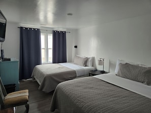Habitación de hotel con dos camas, un escritorio, una silla, una lámpara y una ventana con cortinas.