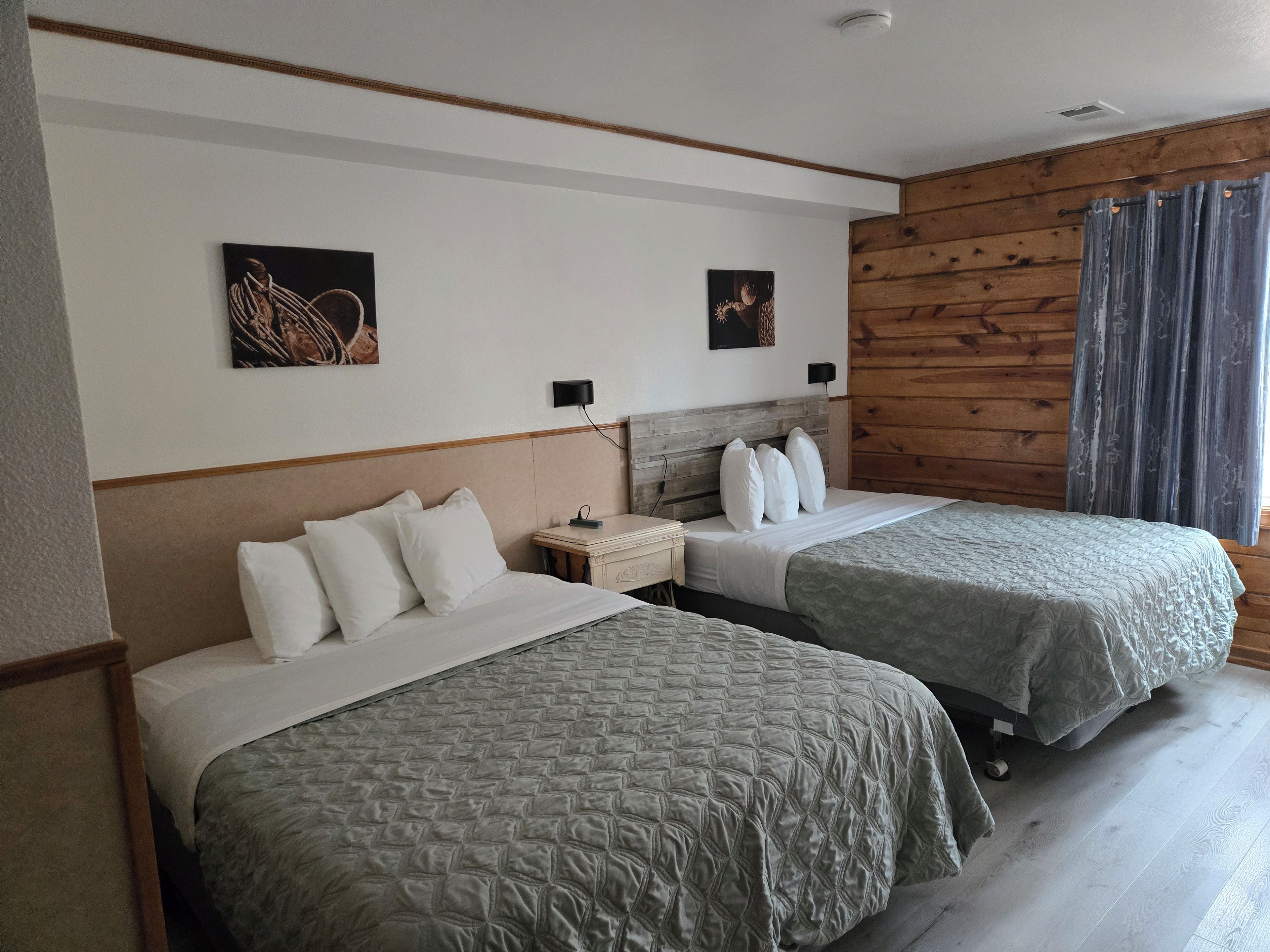 A hotel room with two beds, a wooden headboard, a nightstand, and two wall-mounted lamps.