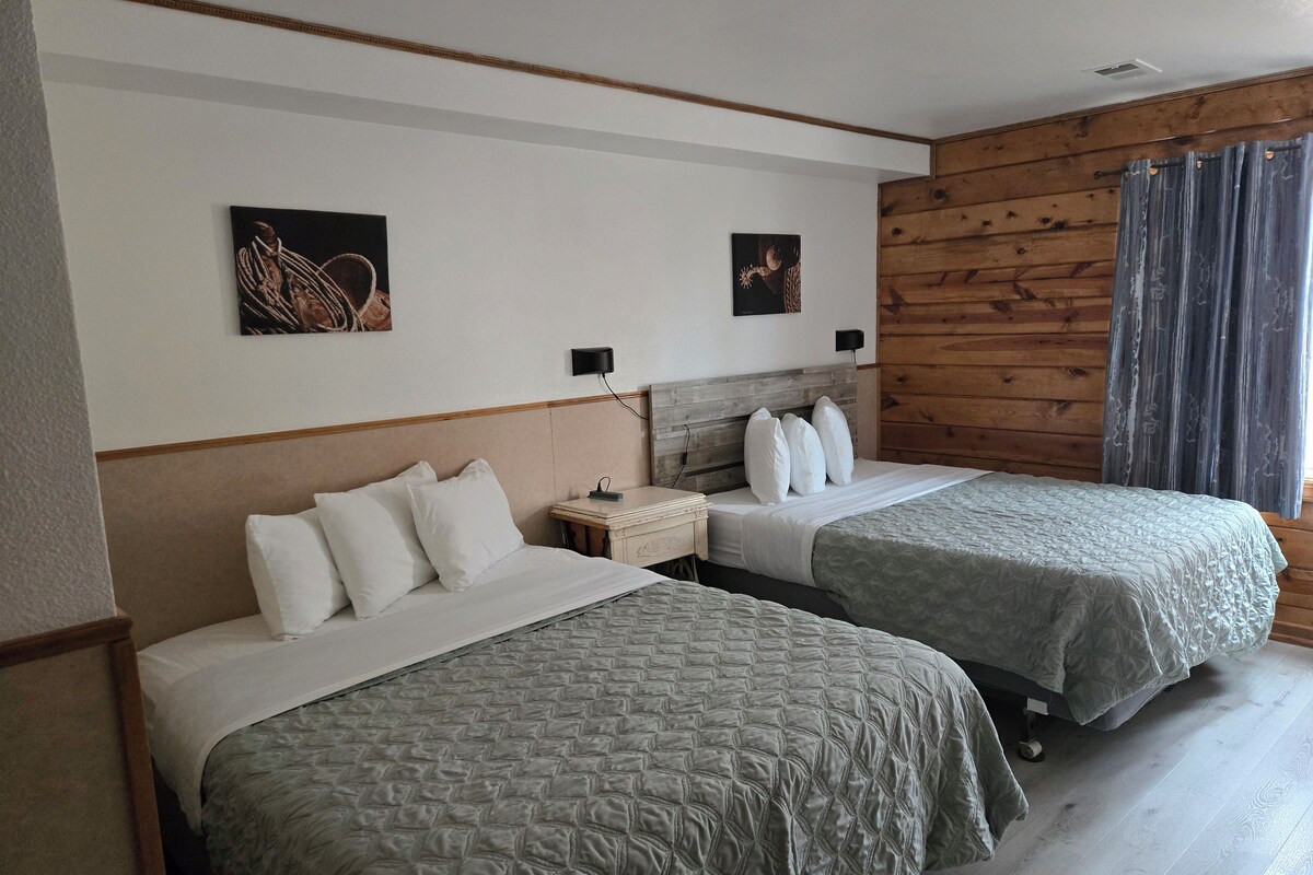 Habitación de hotel con dos camas, cabecero de madera, mesita de noche y dos lámparas fijadas a la pared.