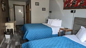 Habitación de hotel con dos camas, un escritorio, una silla, un cesto de basura y un cuadro en la pared.