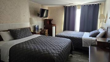 Habitación de hotel con dos camas, un televisor de pantalla plana montado en la pared, un escritorio con lámpara y una ventana con cortinas.