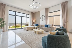 Ampla sala de estar com uma janela grande, conjunto de sofás, mesa de centro e luminária moderna.