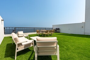 Terraza en la azotea con vistas al mar, amueblada con sillones blancos y una mesa.