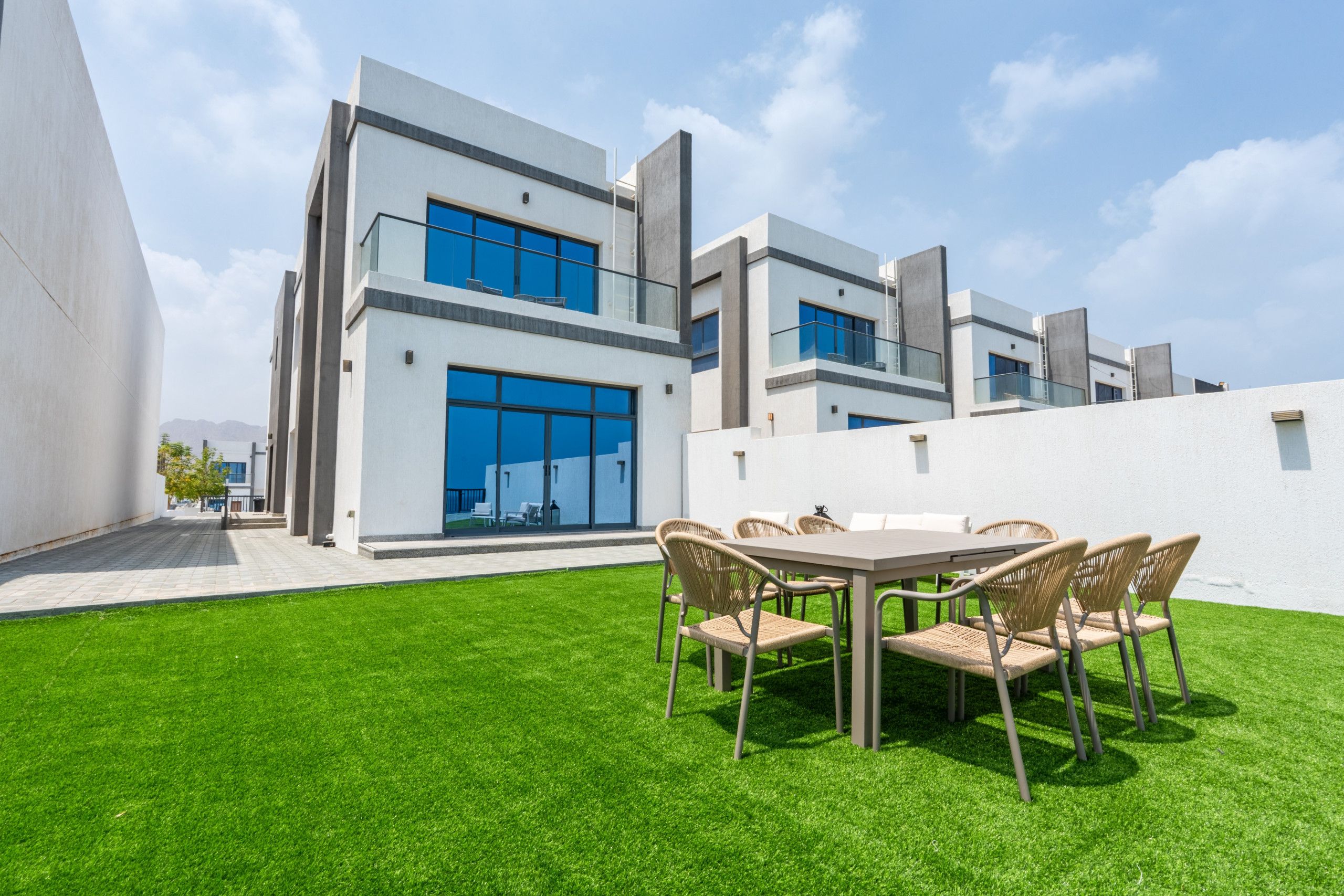 Un edificio moderno con techo plano, ventanas amplias y un césped cuidado con una zona de comedor.