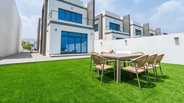 A modern building with a flat roof, large windows, and a well-maintained lawn with a dining area. - Contemporary 4BR Villa with Assistant & Driver Rooms, Gulf Views, BBQ and Outdoor Lounge (Fujairah)