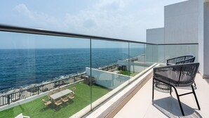 A balcony with a glass railing overlooking the sea, furnished with chairs and a table. - Contemporary 4BR Villa with Assistant & Driver Rooms, Gulf Views, BBQ and Outdoor Lounge (Fujairah)