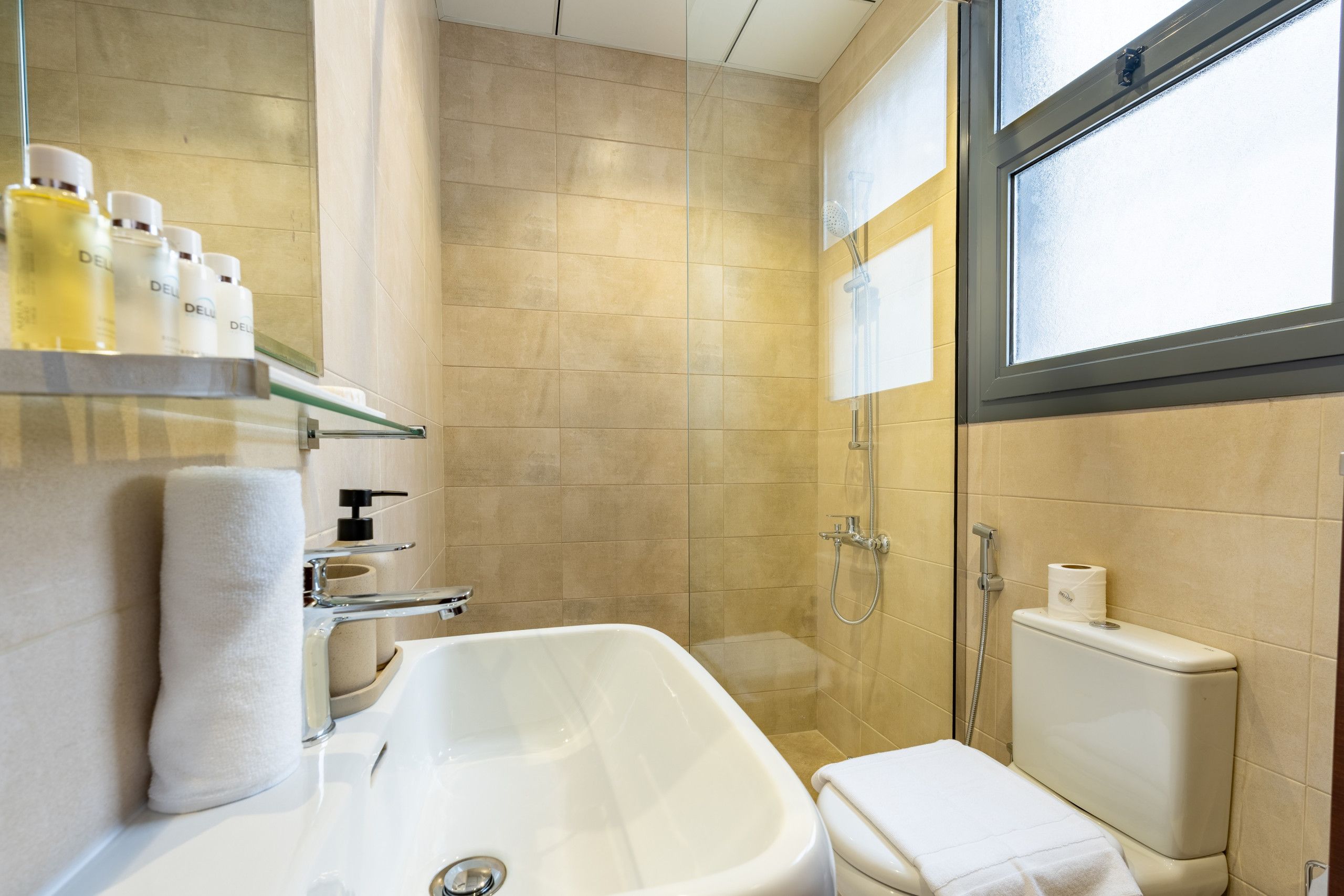 Un baño con una bañera, un inodoro y una ducha. Hay artículos de aseo en un estante y una toalla en el suelo.