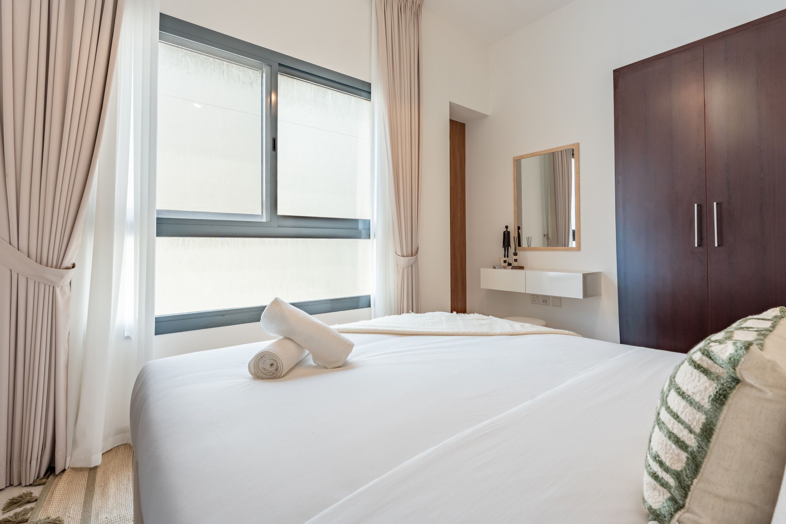 Une chambre d’hôtel avec un grand lit, une fenêtre avec des rideaux, une armoire et un miroir au mur.