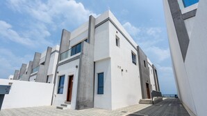 A modern building with a flat roof, large windows, and a paved entrance area. - Contemporary 4BR Villa with Assistant & Driver Rooms, Gulf Views, BBQ and Outdoor Lounge (Fujairah)