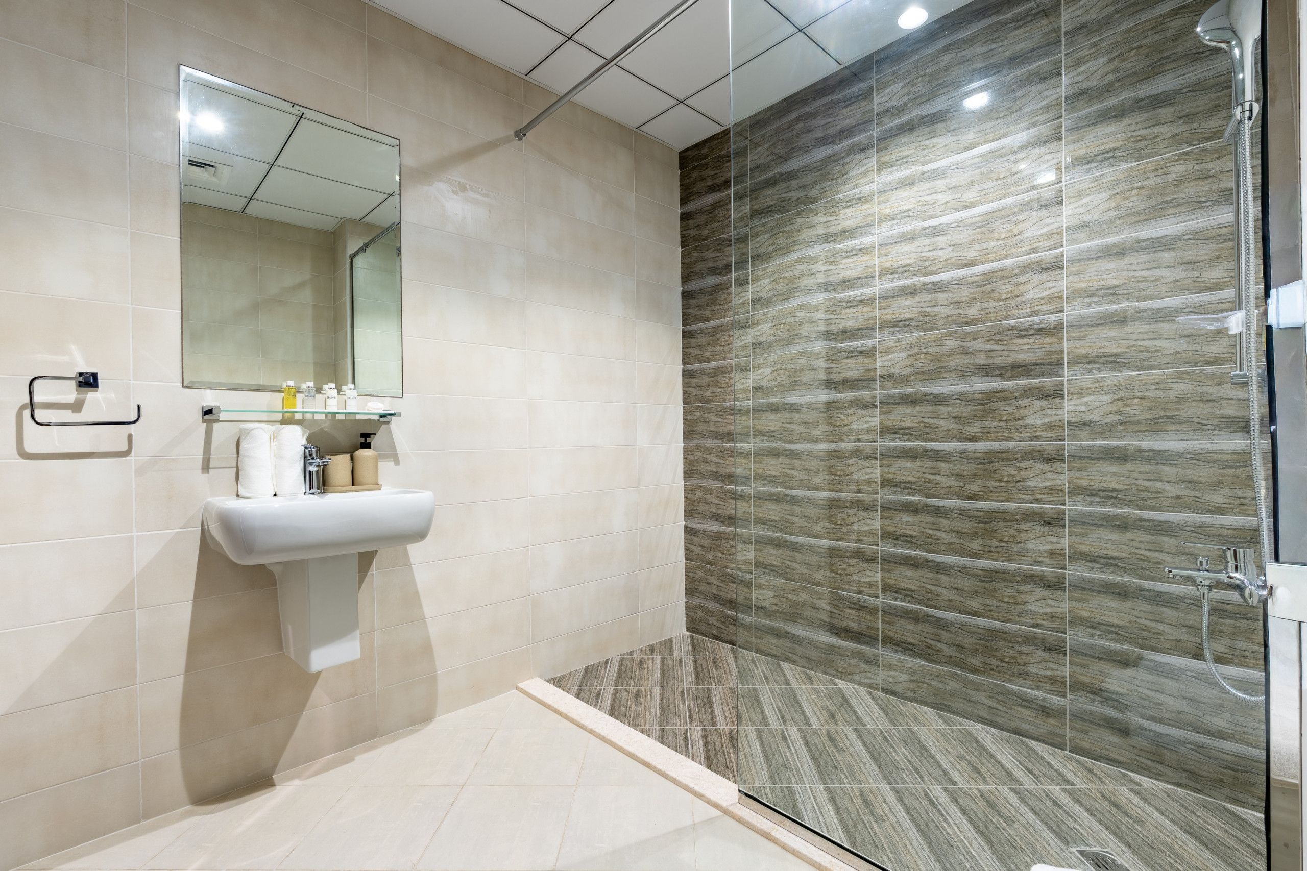 A modern bathroom with a glass shower enclosure, a sink with toiletries, and a mirror.