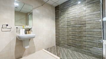 A modern bathroom with a glass shower enclosure, a sink with toiletries, and a mirror.