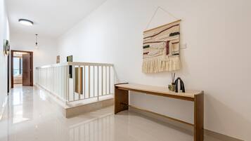 Un pasillo con barandilla blanca, un banco de madera y un tapiz colgado en la pared.