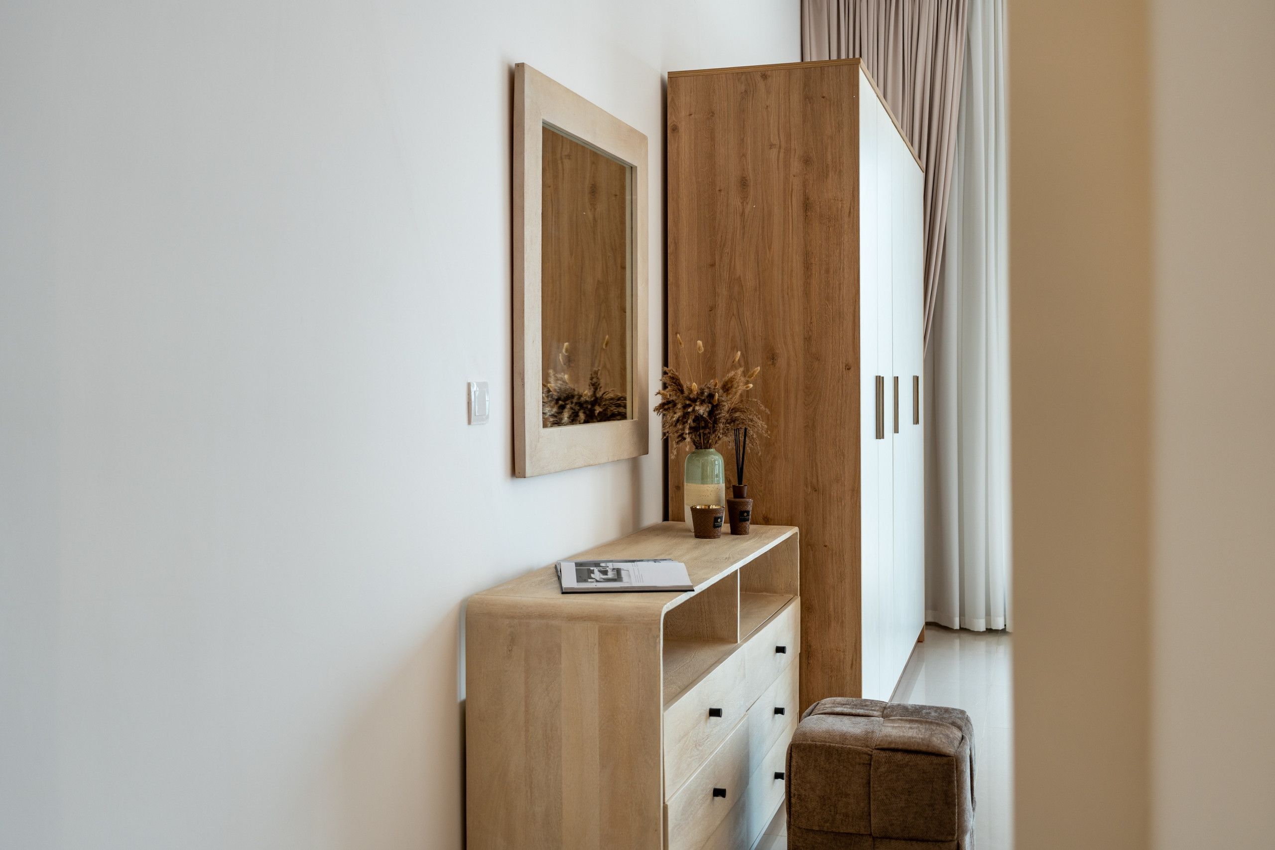 A minimalist room with a wooden wardrobe, a mirror, a small table with a vase and a book, and a bench.
