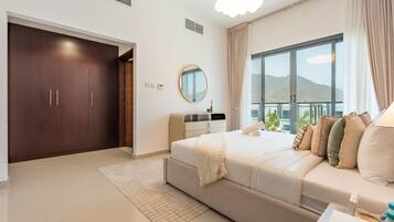 A modern bedroom with a large bed, a dresser, a mirror, and a window with a view of mountains.