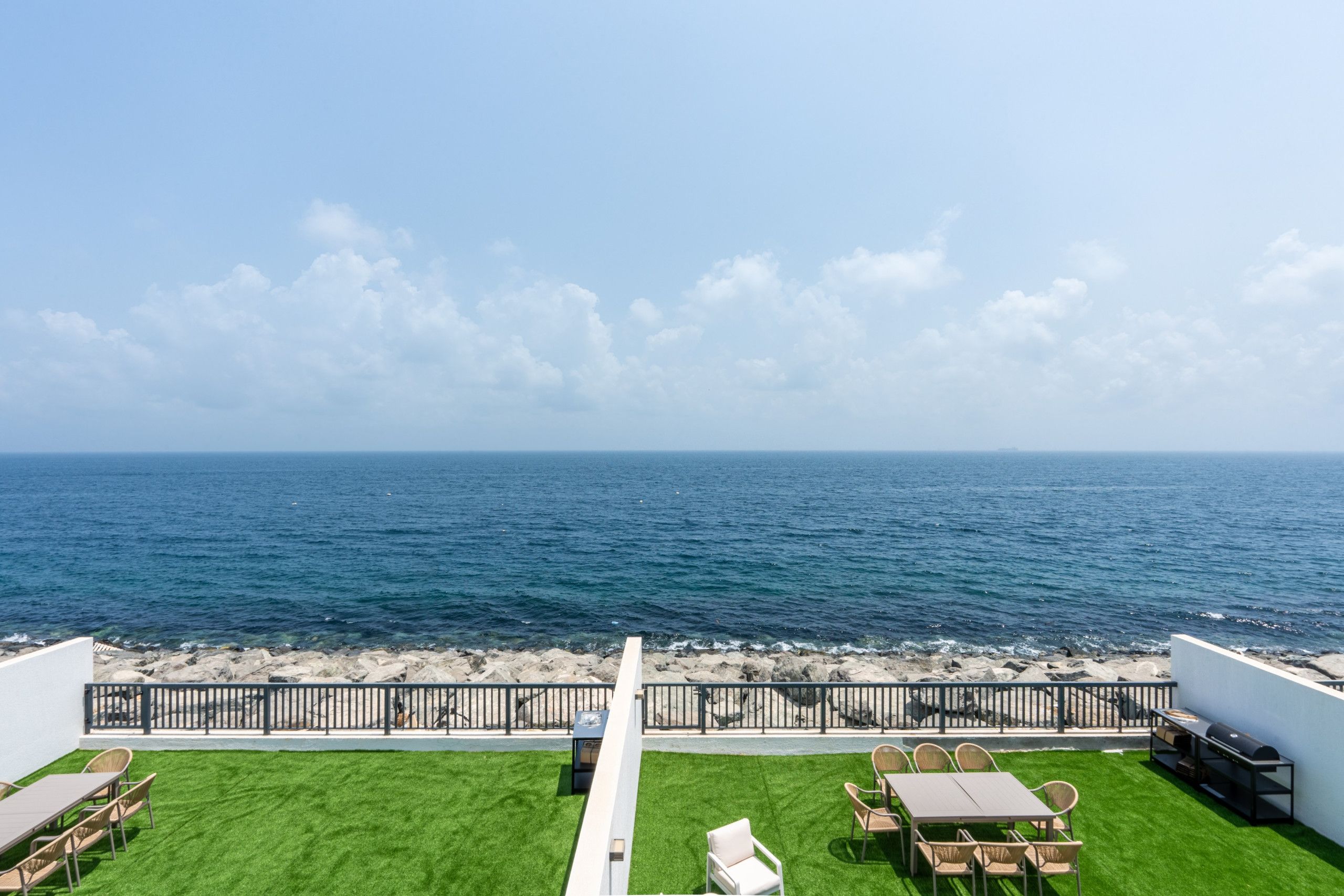Una terraza en la azotea con vistas al mar, amueblada con mesas y sillas, y una parrilla.