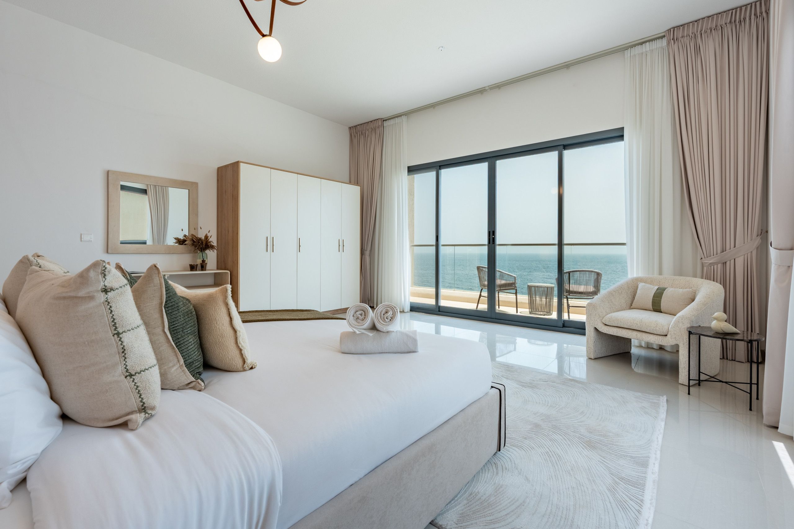 Un dormitorio moderno con una cama grande, un armario, una zona de estar con vistas al mar y un balcón.
