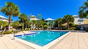 Piscina con sillas de descanso y palmeras, rodeada de edificios.