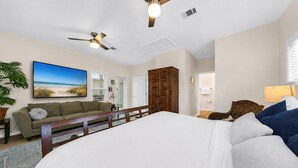 Un dormitorio con una cama grande, cabecera de madera, ventilador de techo y un cuadro con motivos playeros en la pared.