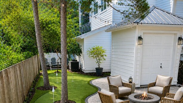Un patio ajardinado con césped artificial, mobiliario de mimbre y un hogar para la chimenea.