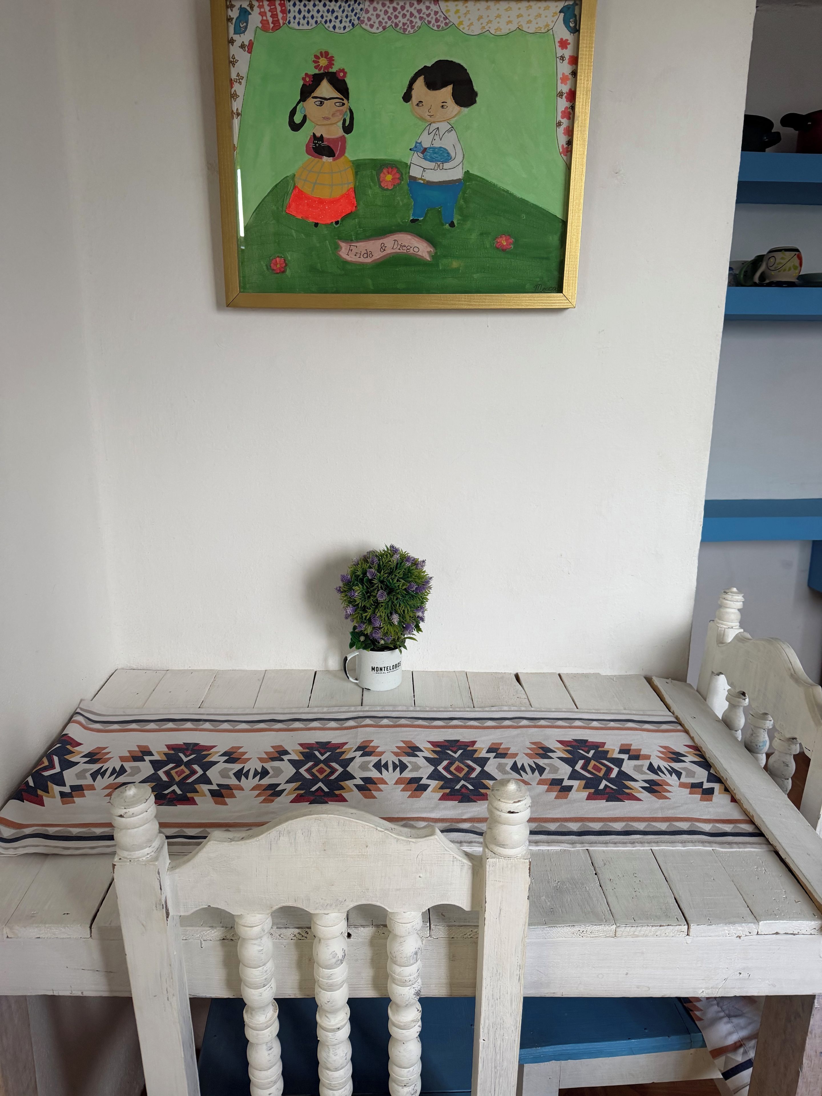 A room with a table, chairs, a framed drawing, and a potted plant.