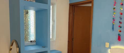 A bedroom with a bed, a blue wardrobe, a desk with a chair, and a window.