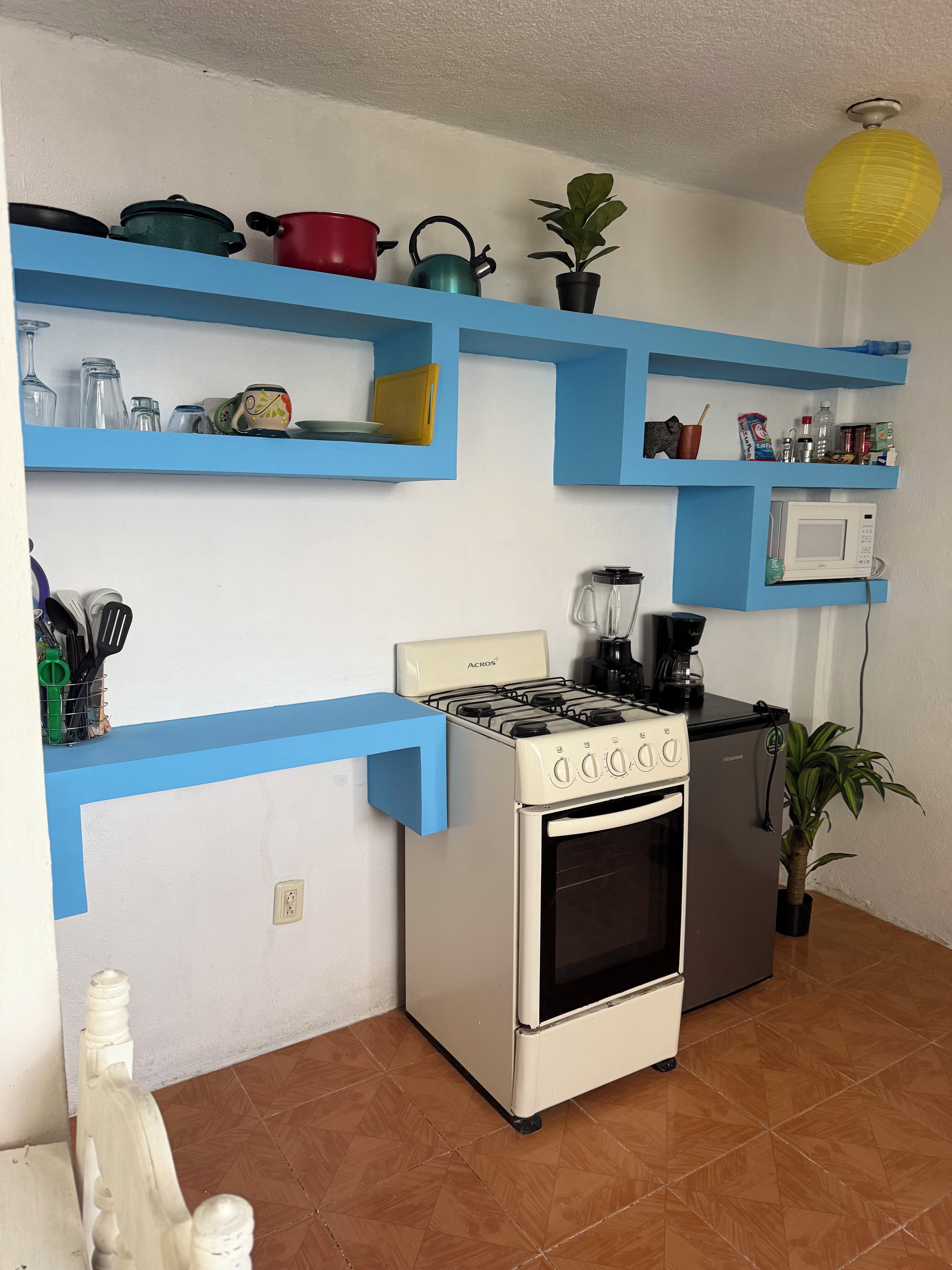 A kitchen with a stove, oven, microwave, and blue shelves with various kitchen items.
