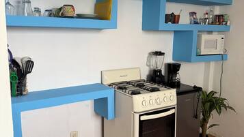 A kitchen with a stove, oven, microwave, and blue shelves with various kitchen items.