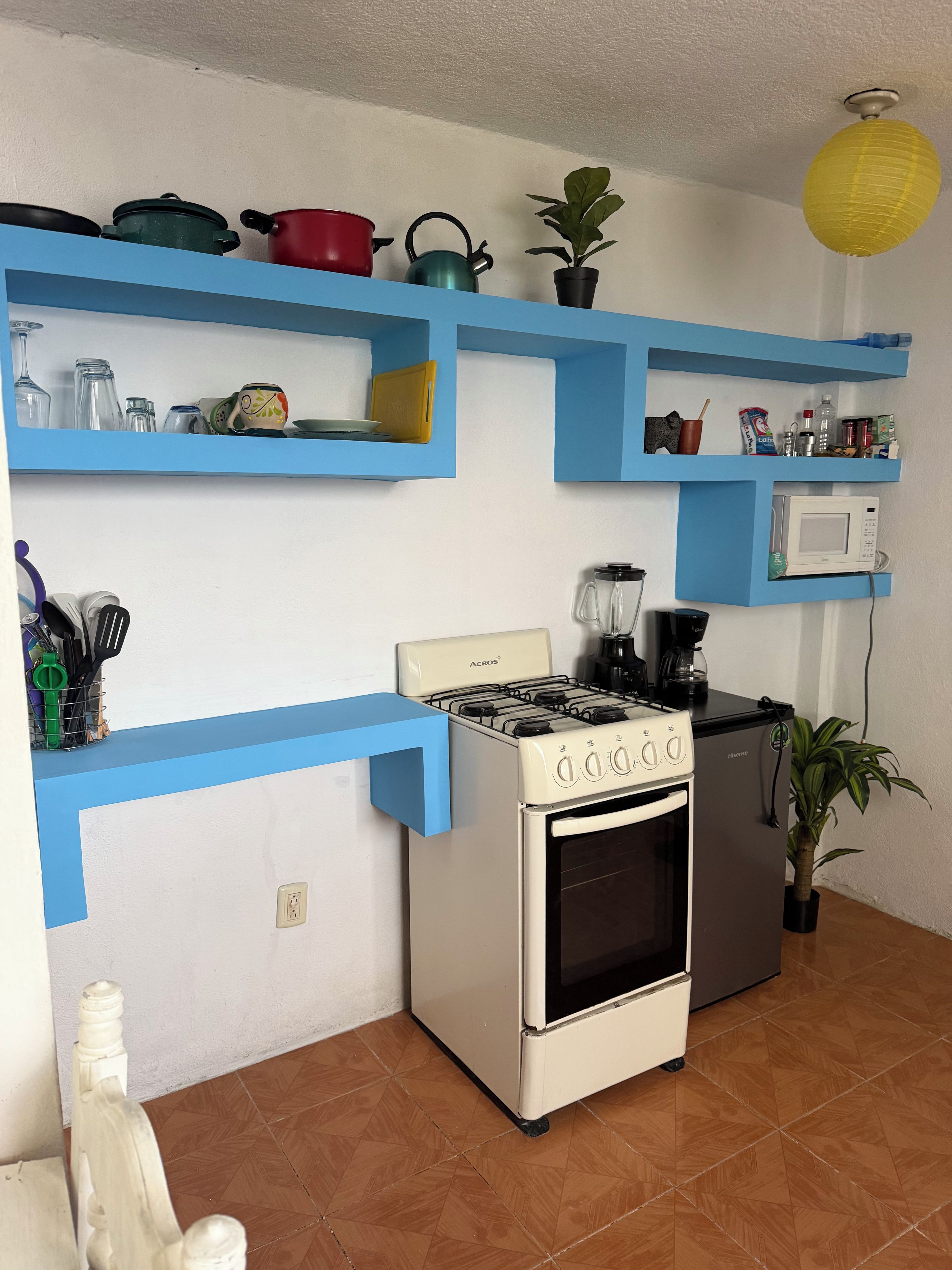 A kitchen with blue shelves, a stove, oven, microwave, and potted plants.