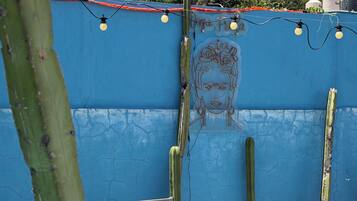 Una pared azul con un jardín de cactus, una silla de metal y una mesa con un objeto decorativo.